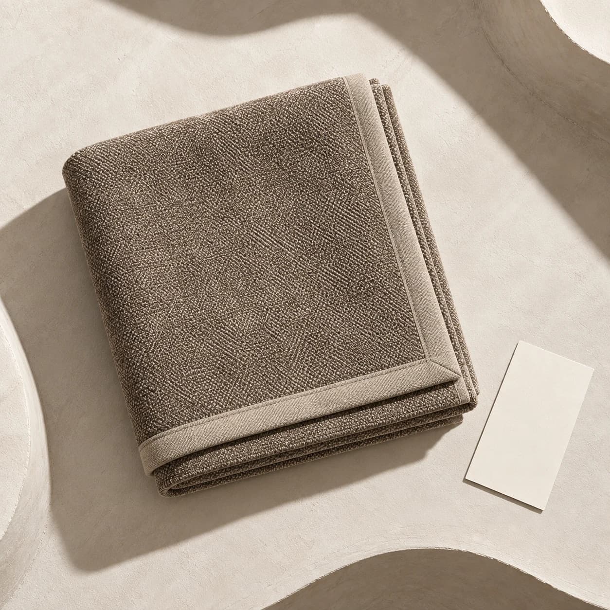 Jeté de canapé en chenille taupe plié sur un fond crème
